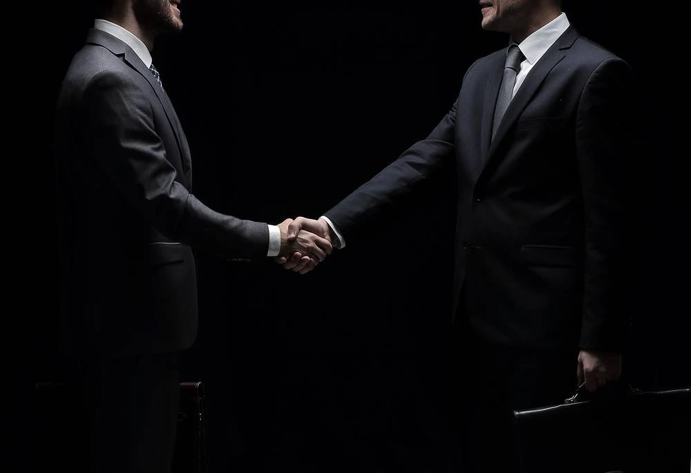 Attorney shaking hands with another man steeped in shadows.